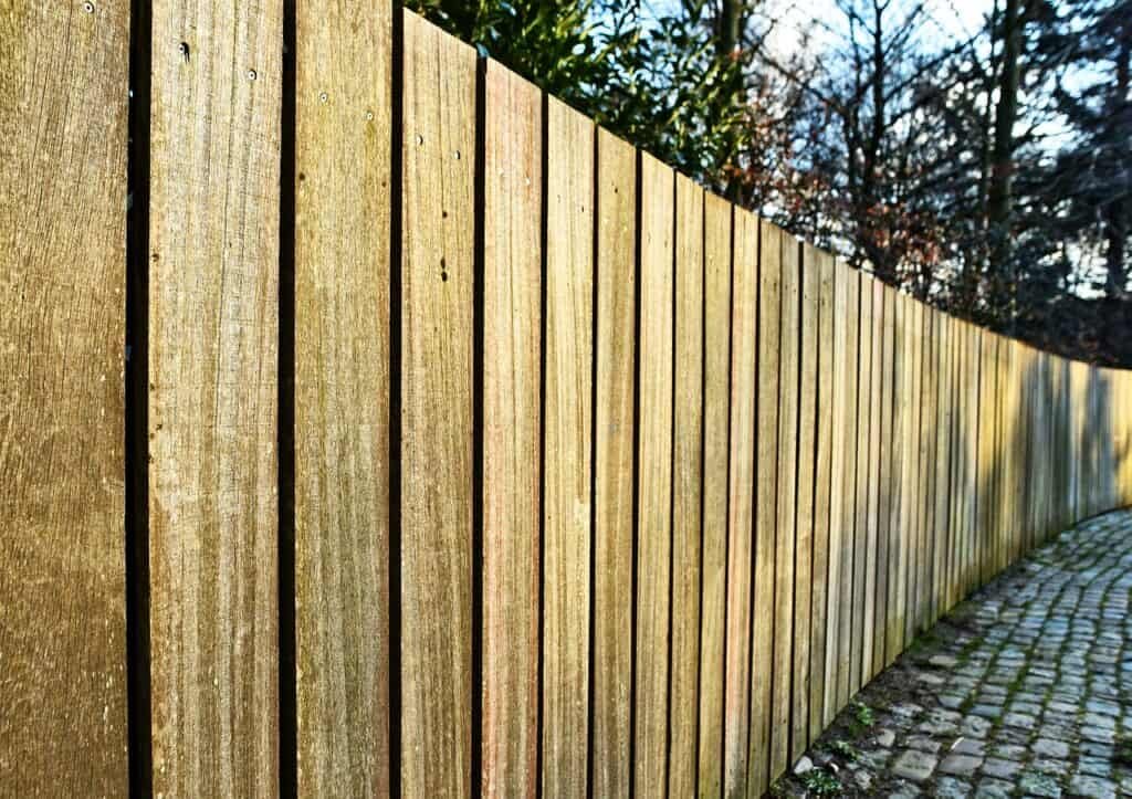 A long wooden fence beside a cobblestone path, with trees in the background.