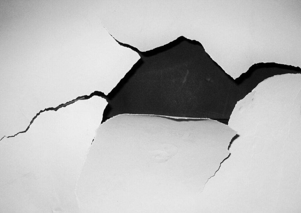 A white drywall crack revealing a dark background.