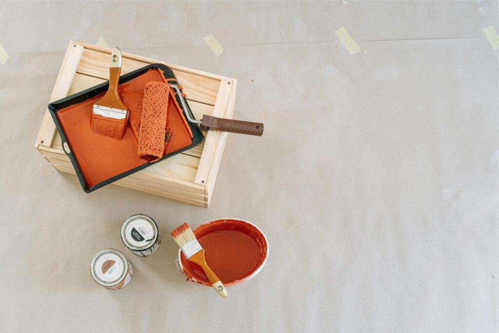 Paint supplies on floor with open paint cans, brush, and roller.